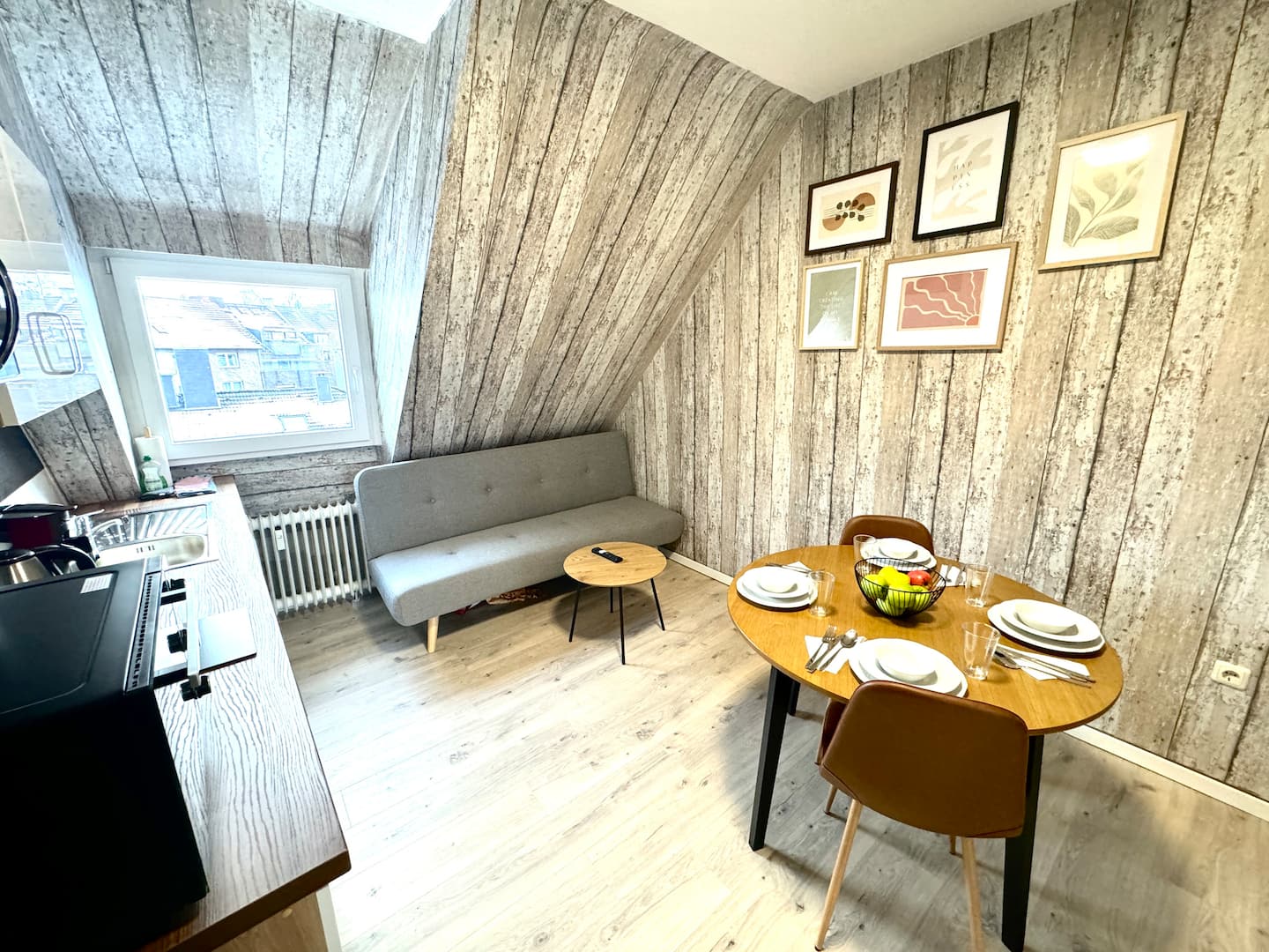 Living area of the renovated studio with couch, dining table and modern wood-look wall